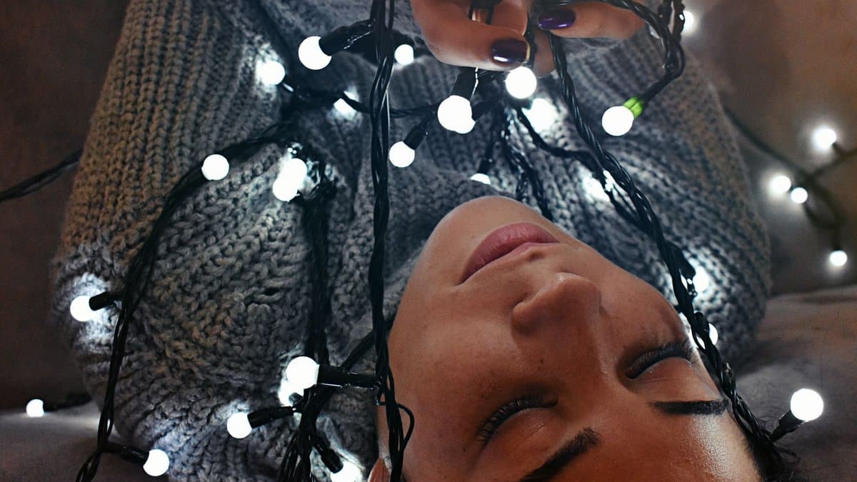 Intimate indoor portrait of a woman wrapped in glowing string lights, evoking warmth and festivity.