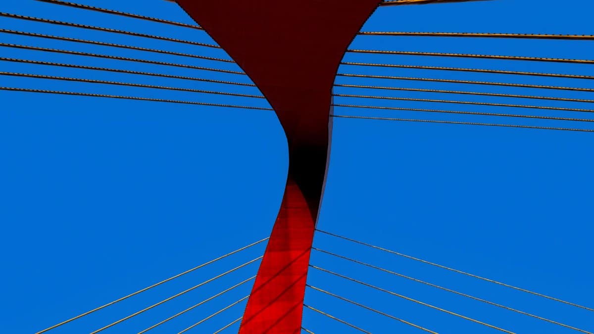 A striking modern bridge with red and blue colors and abstract lines against a clear sky.