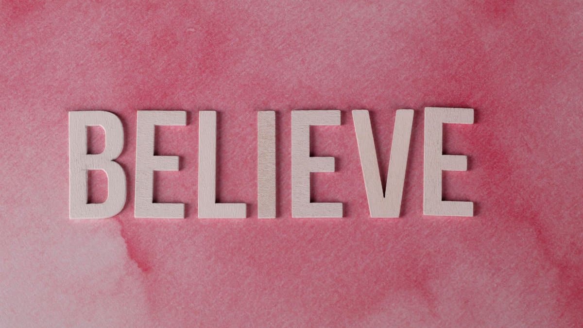 Inspirational word 'Believe' crafted on a textured pink watercolor background. Ideal for motivation.