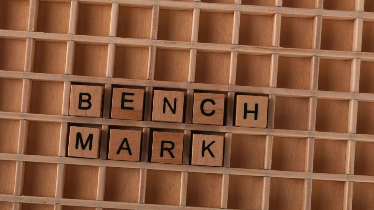 Wooden letter tiles spelling 'BENCHMARK' placed on a grid-like wooden background.