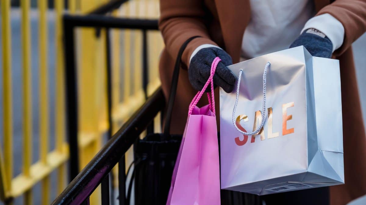 Crop anonymous female in warm coat and gloves looking in shopping bags with purchases while standing on city street on spring day