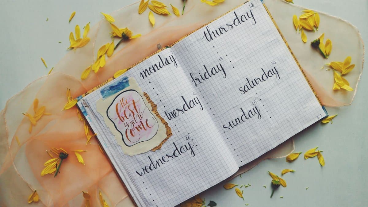 Open planner with days of the week, surrounded by yellow petals and an inspiring quote.
