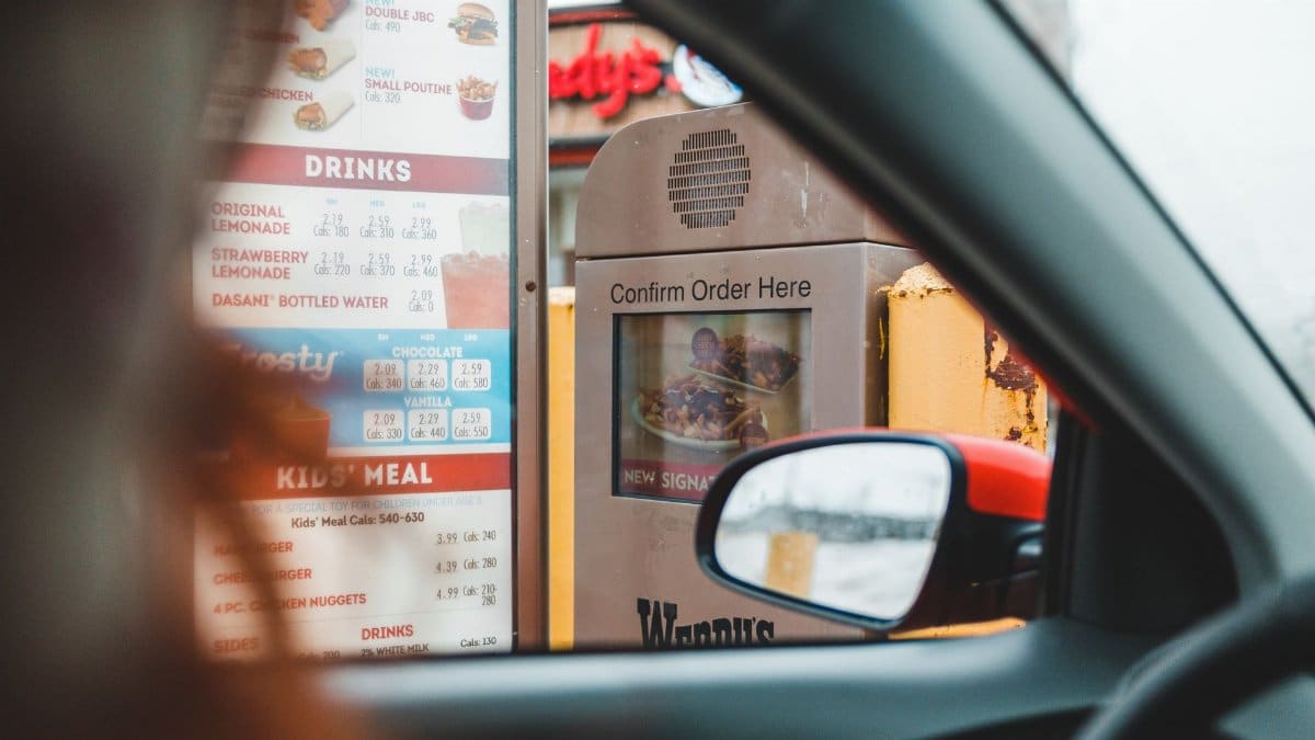 Blurred driver choosing food from menu and telling order to drive thru speaker post