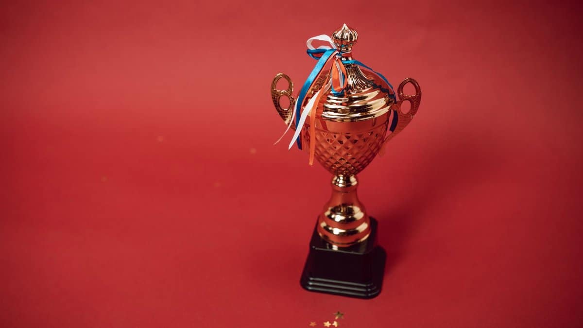 Golden trophy cup with red, blue, and white ribbons on a red backdrop symbolizes achievement and success.
