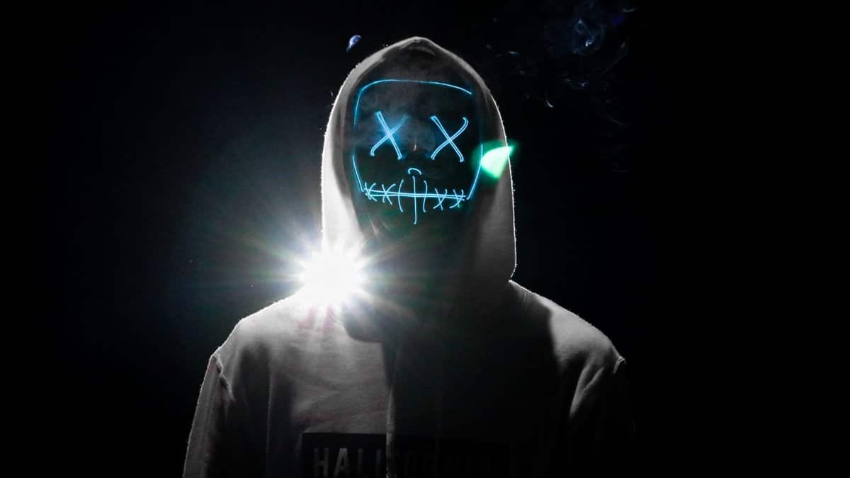 A lone figure in a hoodie wearing a glowing LED purge mask, creating an eerie Halloween vibe.