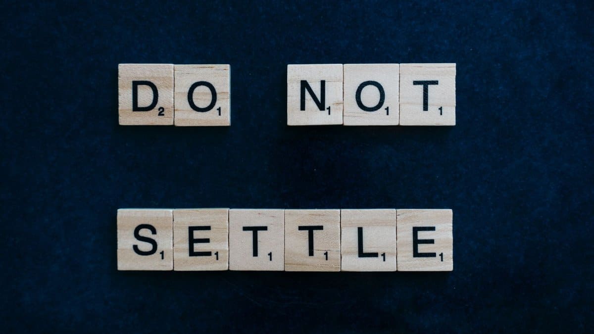 Wooden Scrabble tiles spelling 'Do Not Settle' on a dark surface, top view.