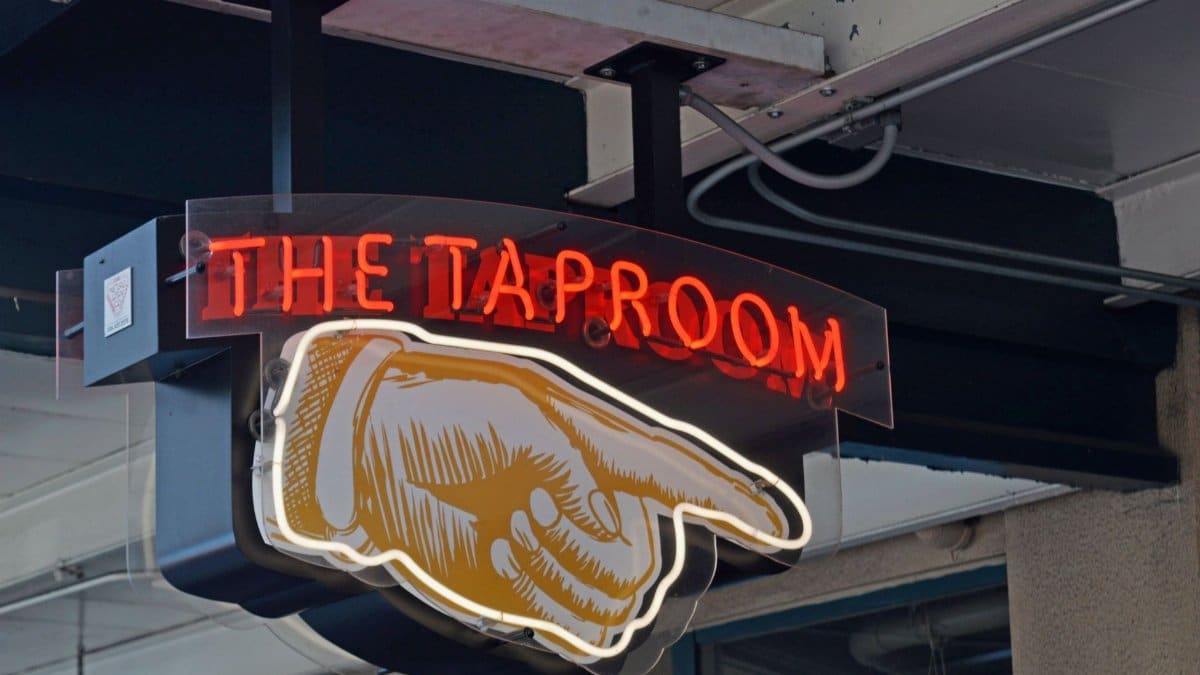 Low angle of illuminated signboard of taproom showing direction with forefinger on city street
