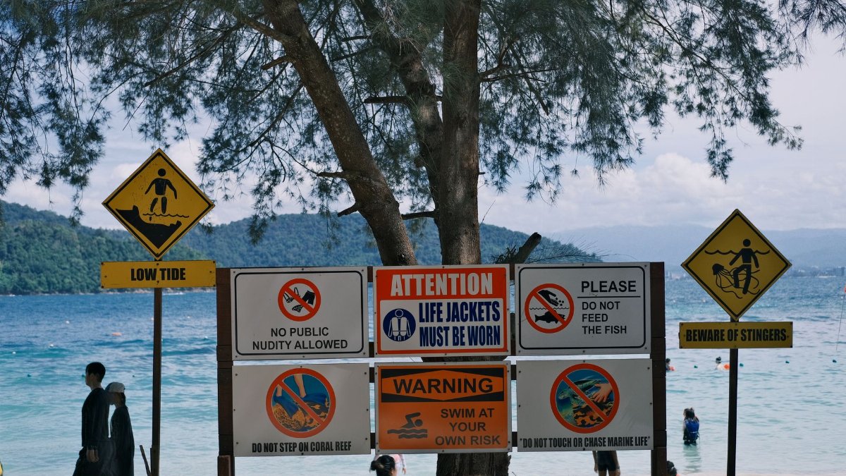 Various safety signs on a beach indicating swimming precautions and marine warnings.