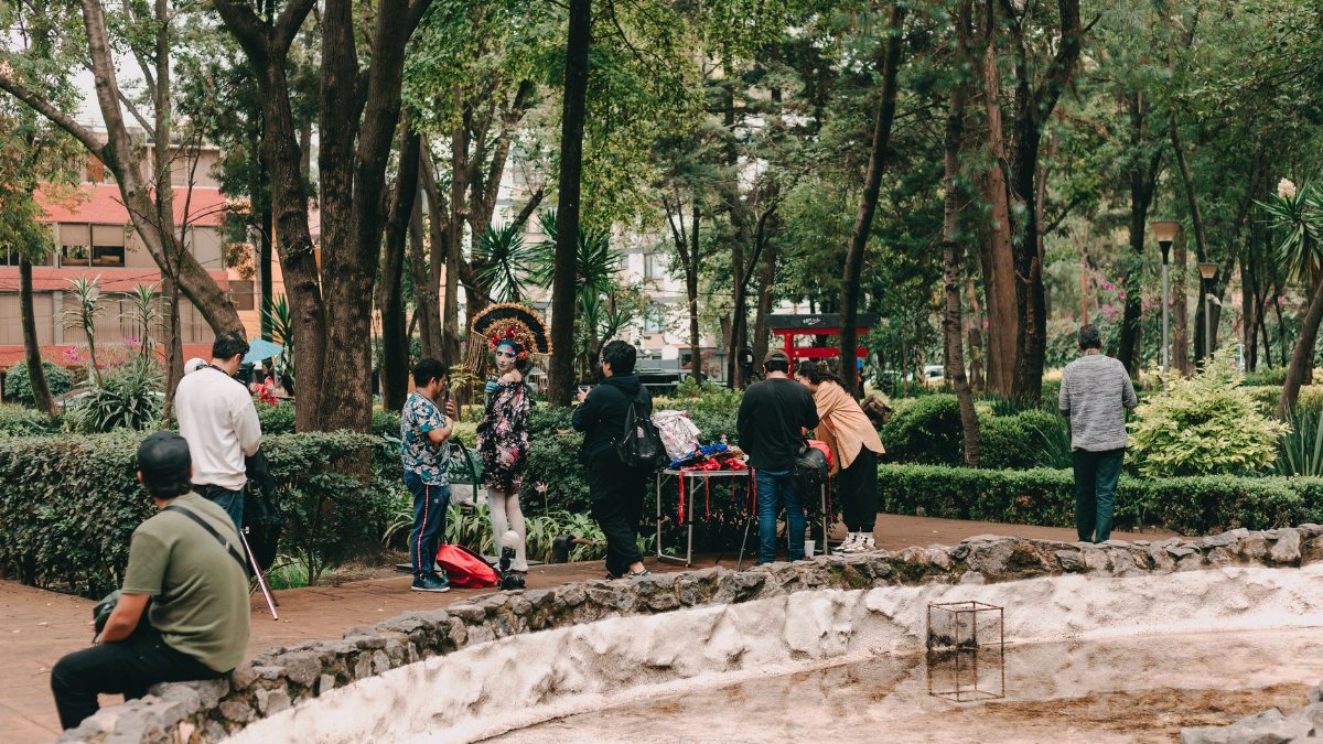 People gathered in a park setting with trees and greenery, engaging in casual social interaction.