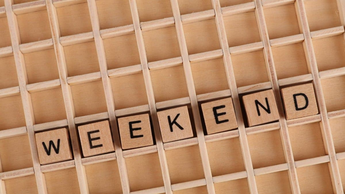 Wooden blocks spelling 'WEEKEND' on a wooden grid surface, minimalist design.