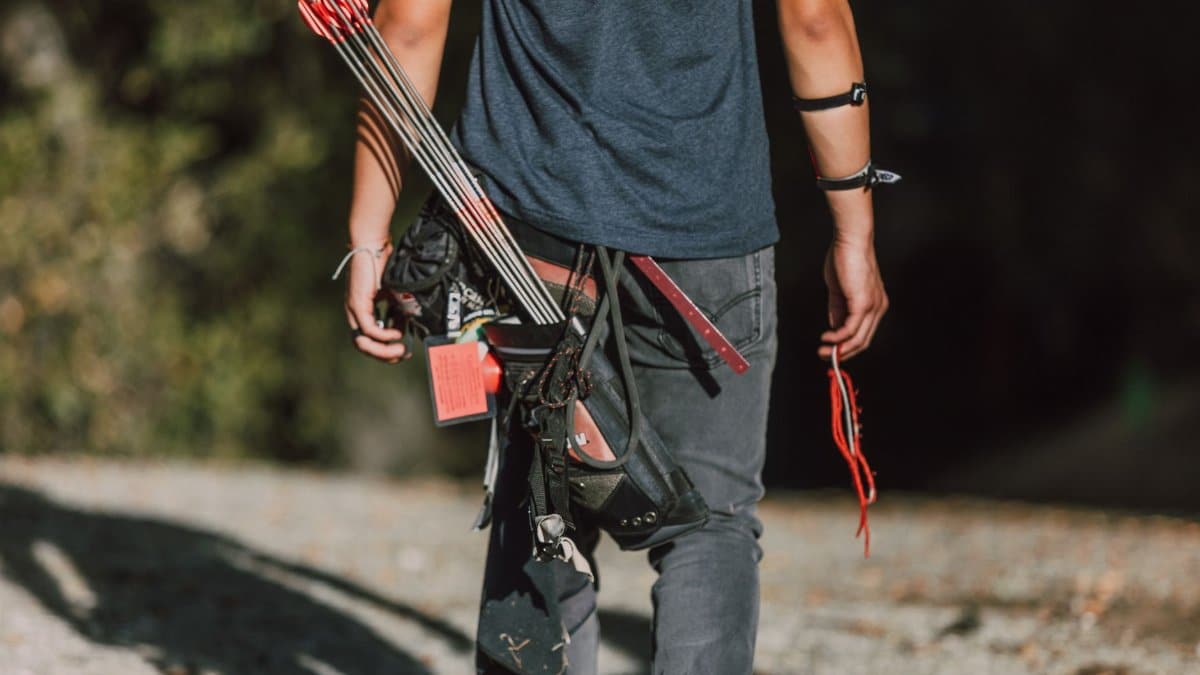 A young archer with arrows and quiver walking outdoors in sunny weather.