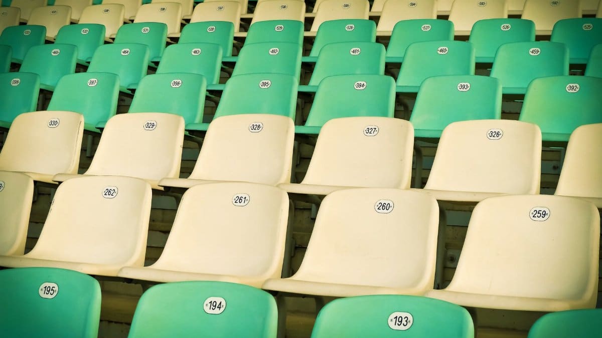 Rows of empty, numbered plastic seats in vibrant green and cream colors at a stadium.
