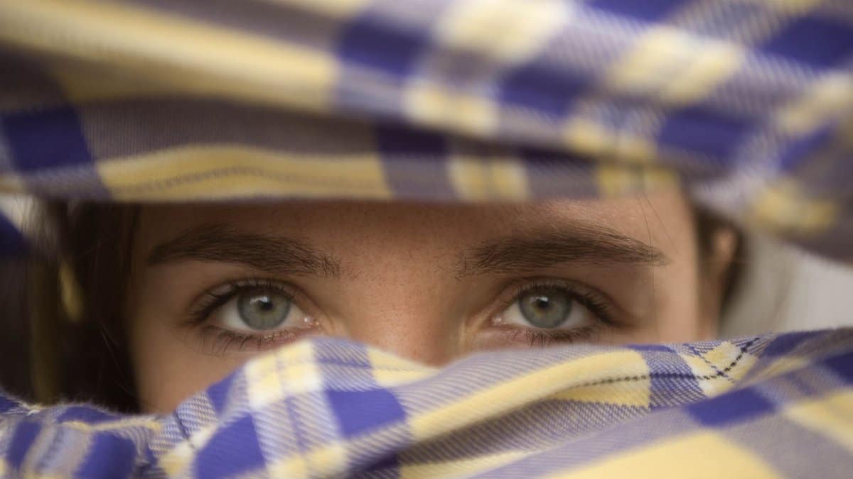 Artistic close-up portrait of woman's eyes peeking through plaid fabric.