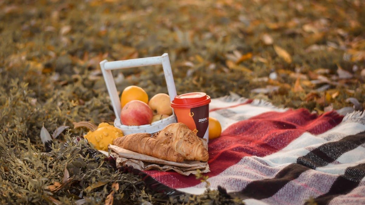 A cozy outdoor picnic setup with croissants, fruits, and coffee on a warm autumn day.