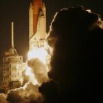 Dramatic capture of a space shuttle launching into the night sky, shrouded in smoke.
