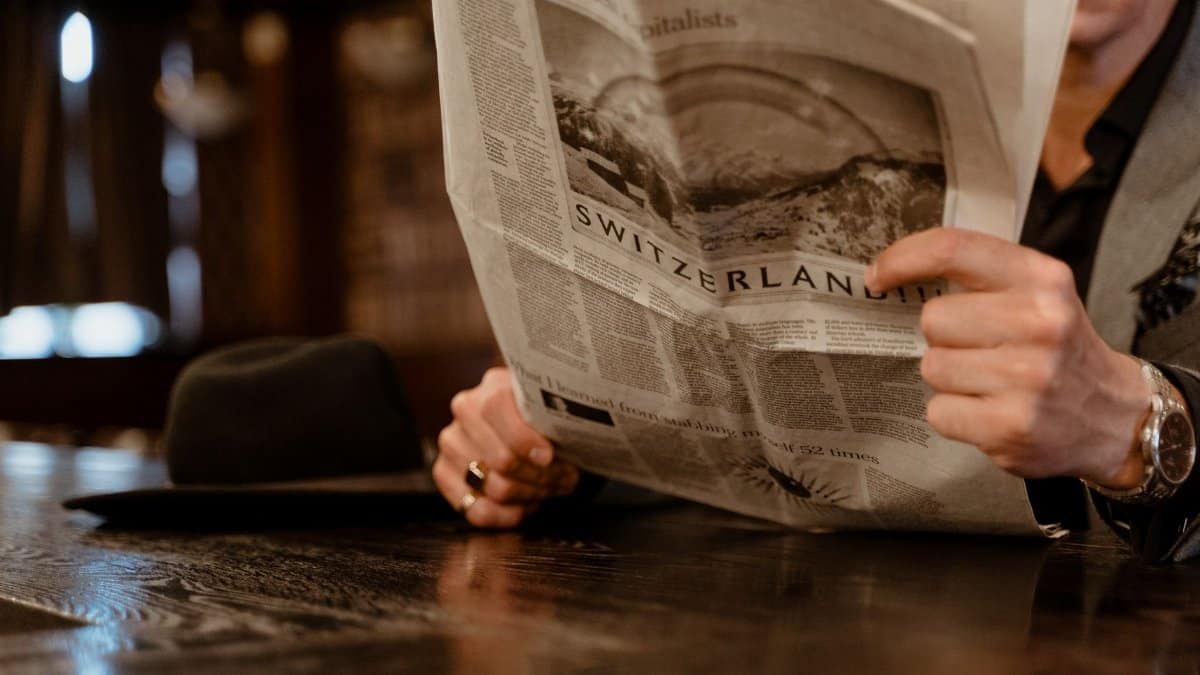 Close-up of man reading newspaper with focus on Switzerland headline.
