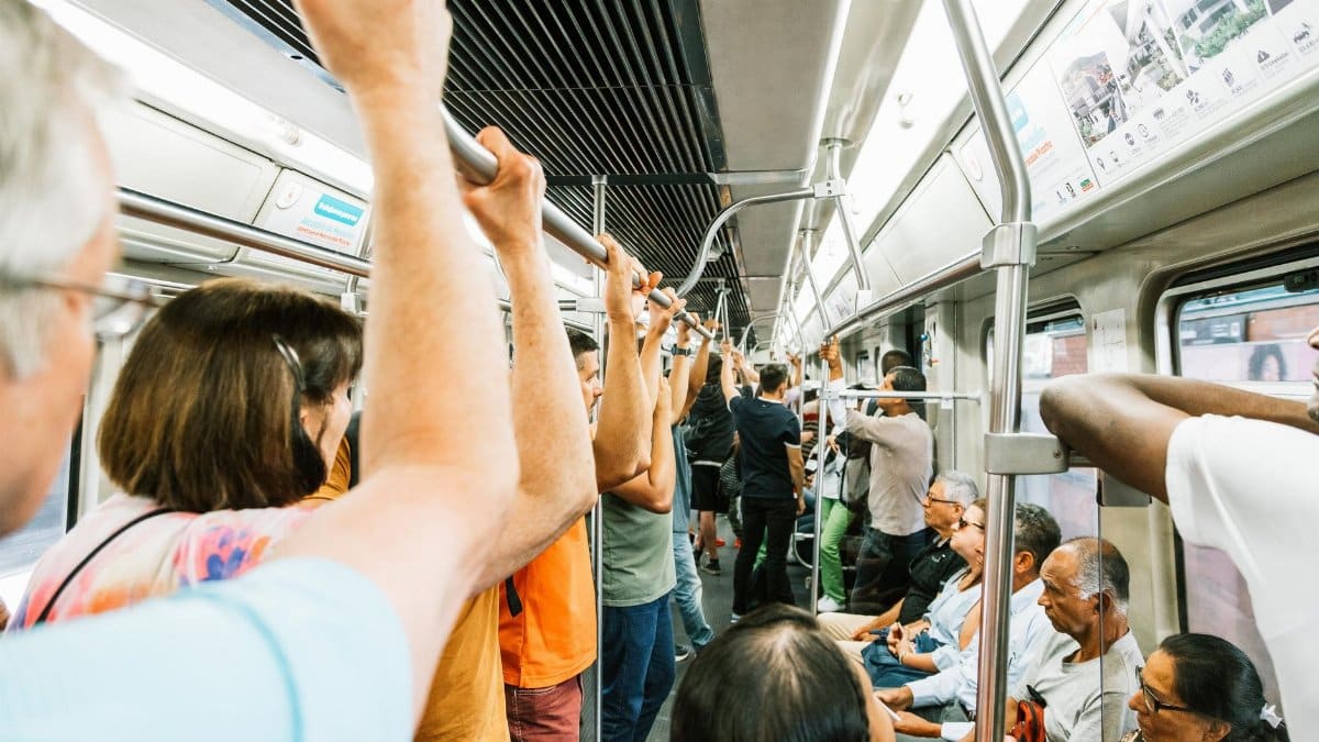 Metro train with sitting and standing passengers with hands on handrail during busy day in town