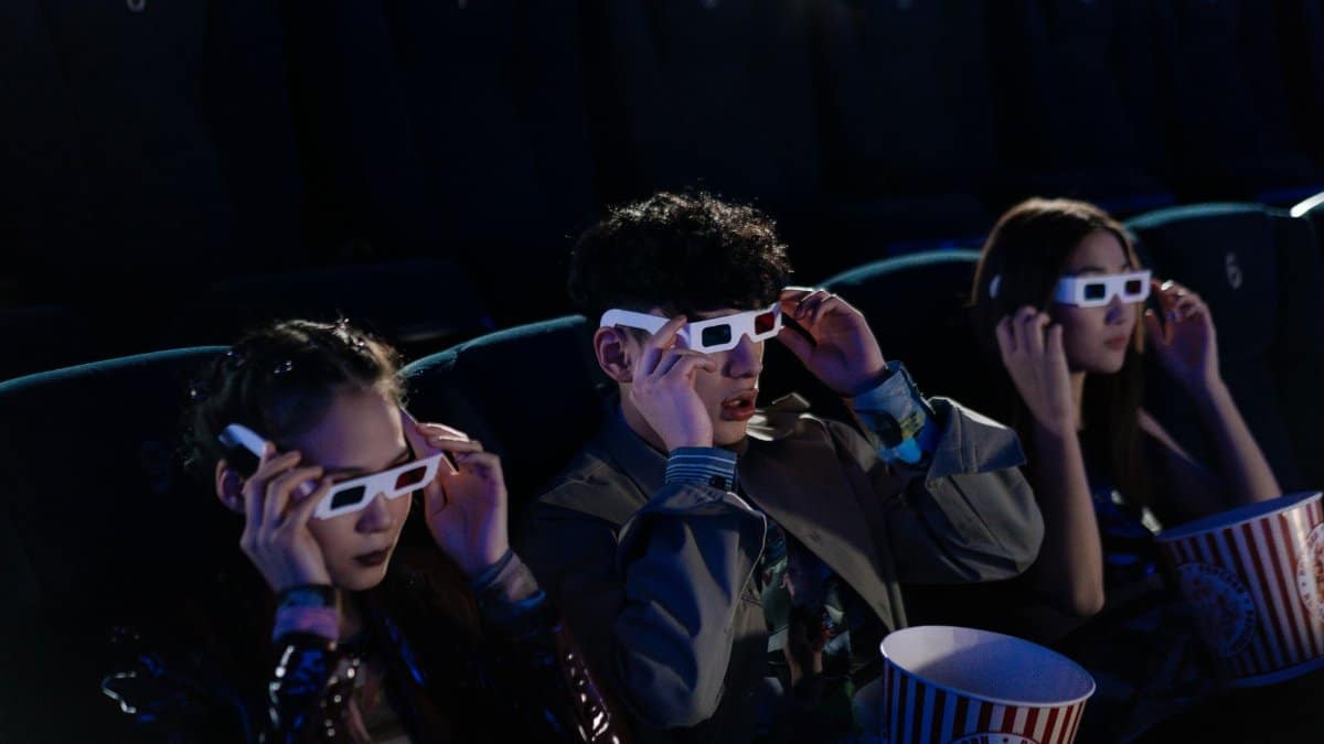 Three people in 3D glasses enjoying a movie at a cinema with popcorn.