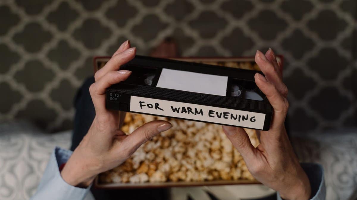 Hands holding a vintage VHS tape labeled 'For Warm Evening' with popcorn in the background.