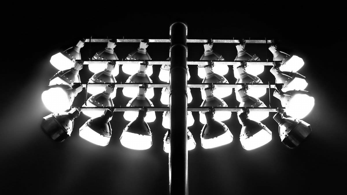 Monochrome image of illuminated floodlights against a dark nighttime sky.