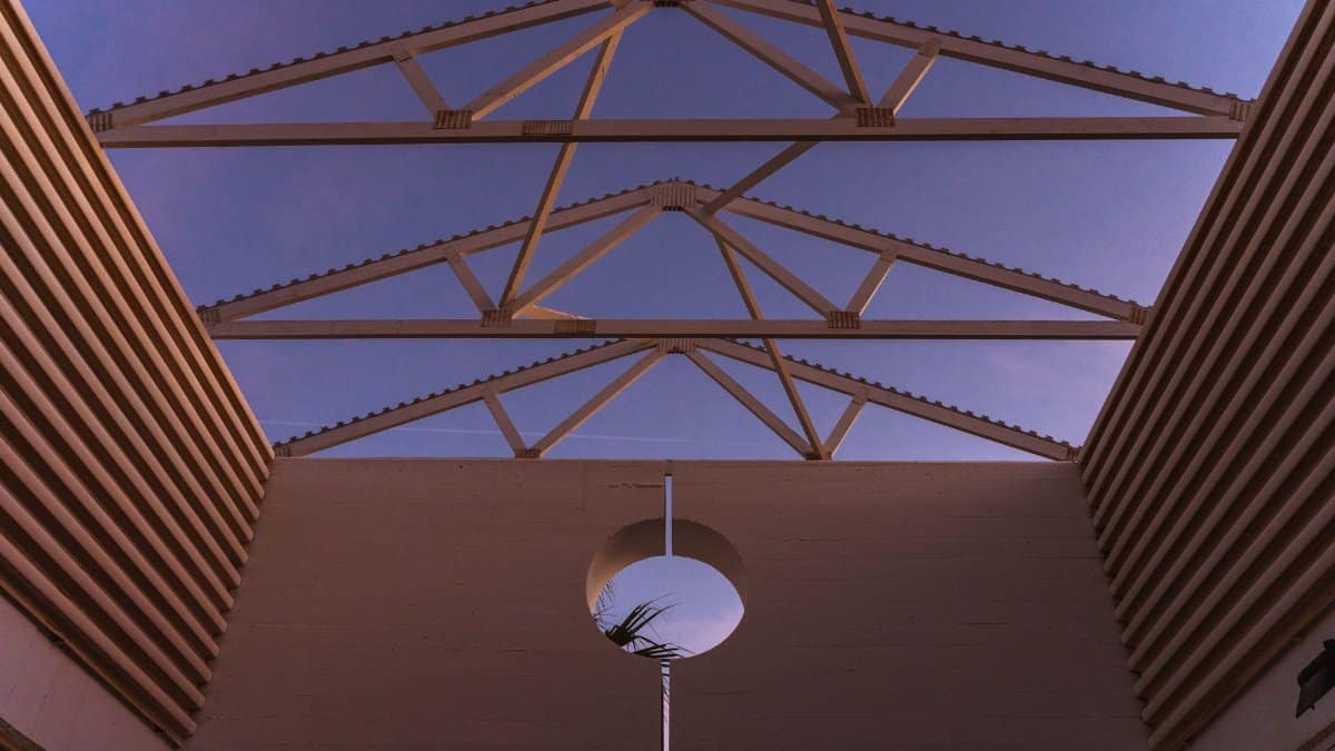 From below of contemporary building with ribbed walls and creative geometric construction on roof against purple sunset sky