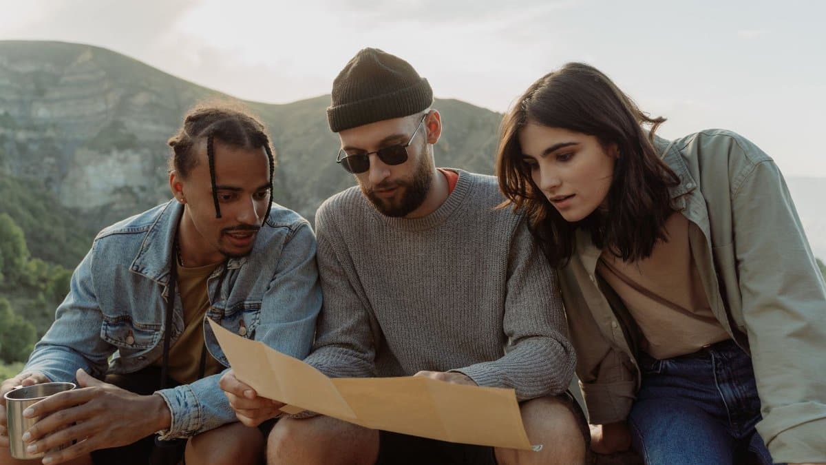 Three young adults studying a map while hiking in the mountains on a sunny day.