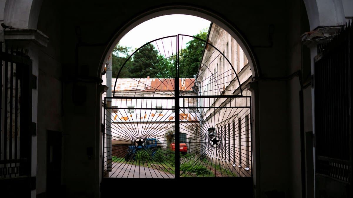View through a decorative metal gate towards a historic courtyard with vehicles