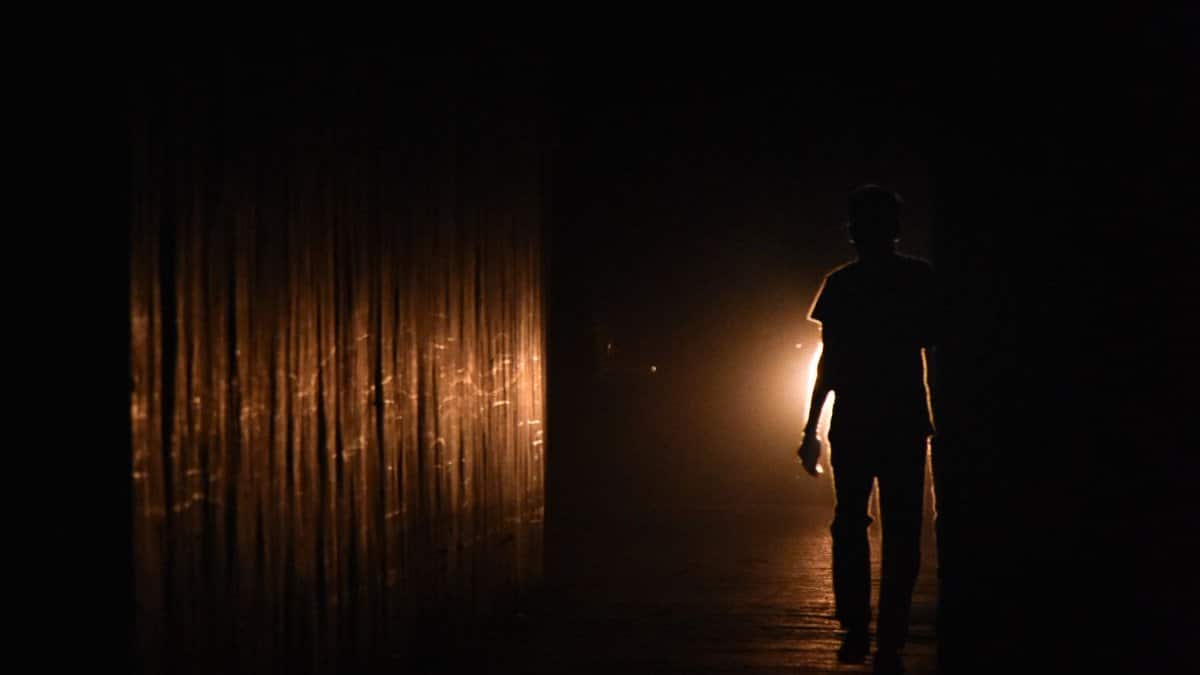 Silhouette of a person walking in a dark hallway illuminated by warm light.