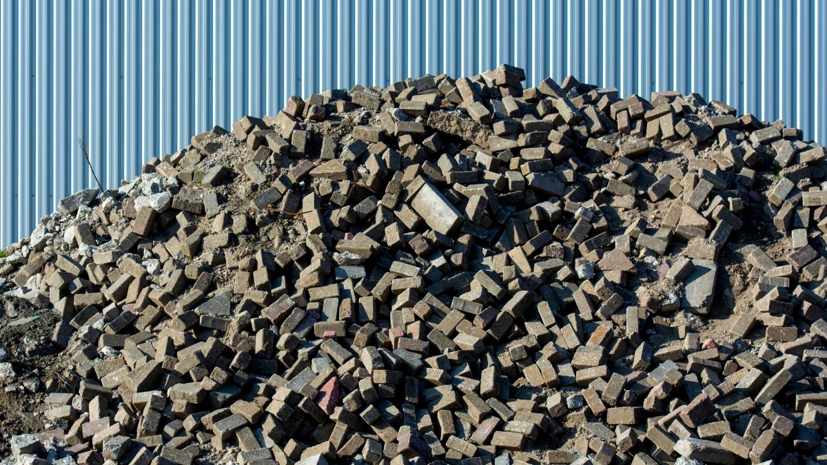 A large pile of rubble consisting of bricks and debris against a corrugated metal fence.