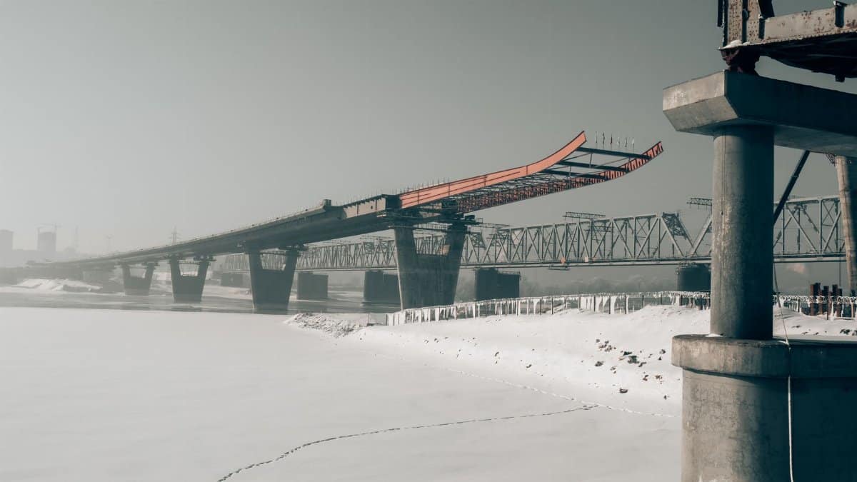 Winter scene of bridge construction over icy river in Novosibirsk, Russia. Snow-covered landscape, industrial setting.