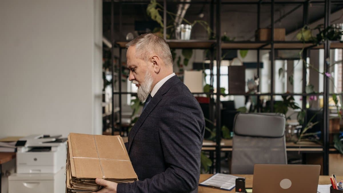 Senior businessman in office attire organizing a stack of documents in a modern office setting.