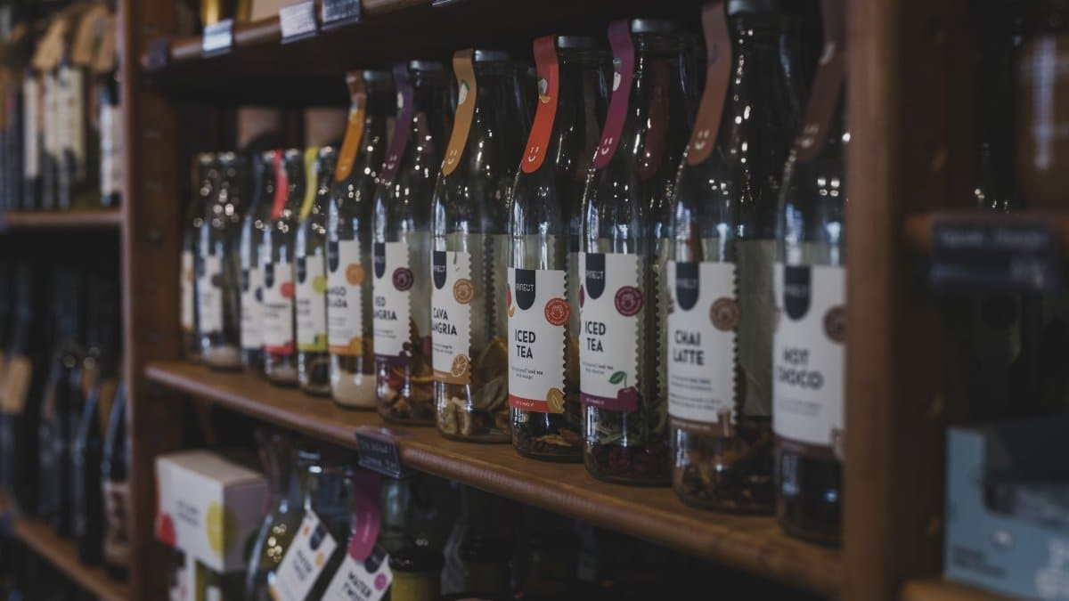 A variety of bottled beverages arranged on wooden shelves in a cozy shop setting.