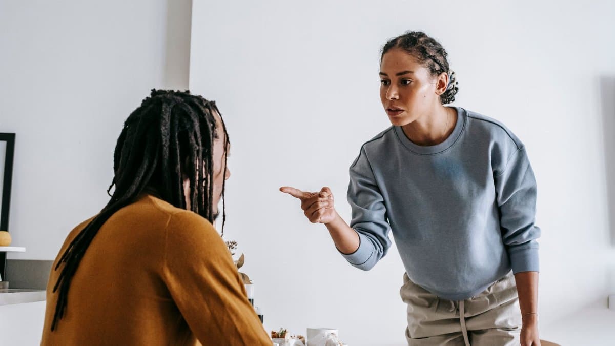 Young African American female standing near table while male sitting at kitchen and having argument