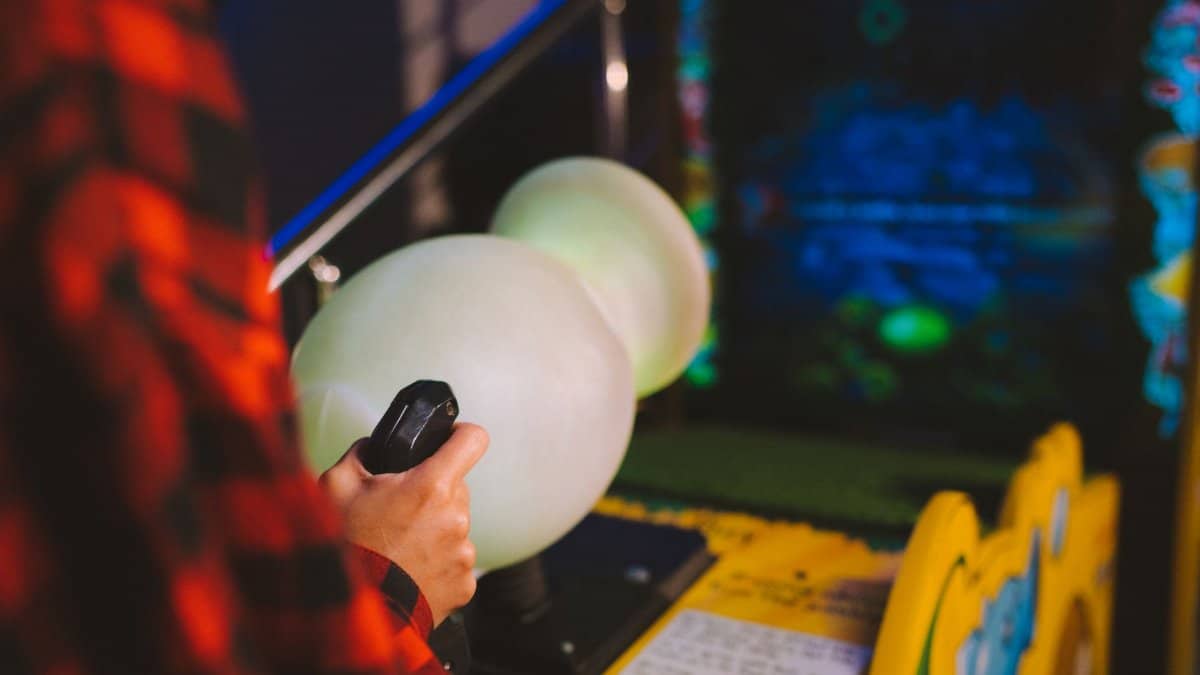 Close-up of a person playing an arcade machine with vibrant lights in a gaming arcade.