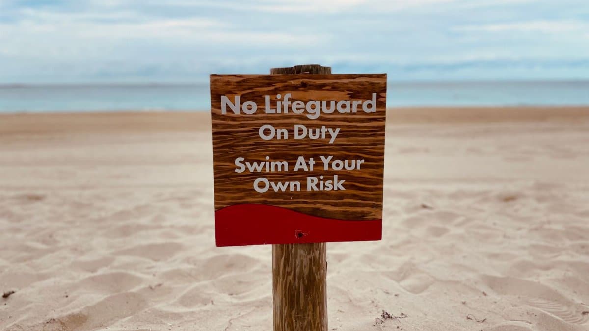 A sandy beach with a sign warning 'No Lifeguard On Duty - Swim At Your Own Risk.'