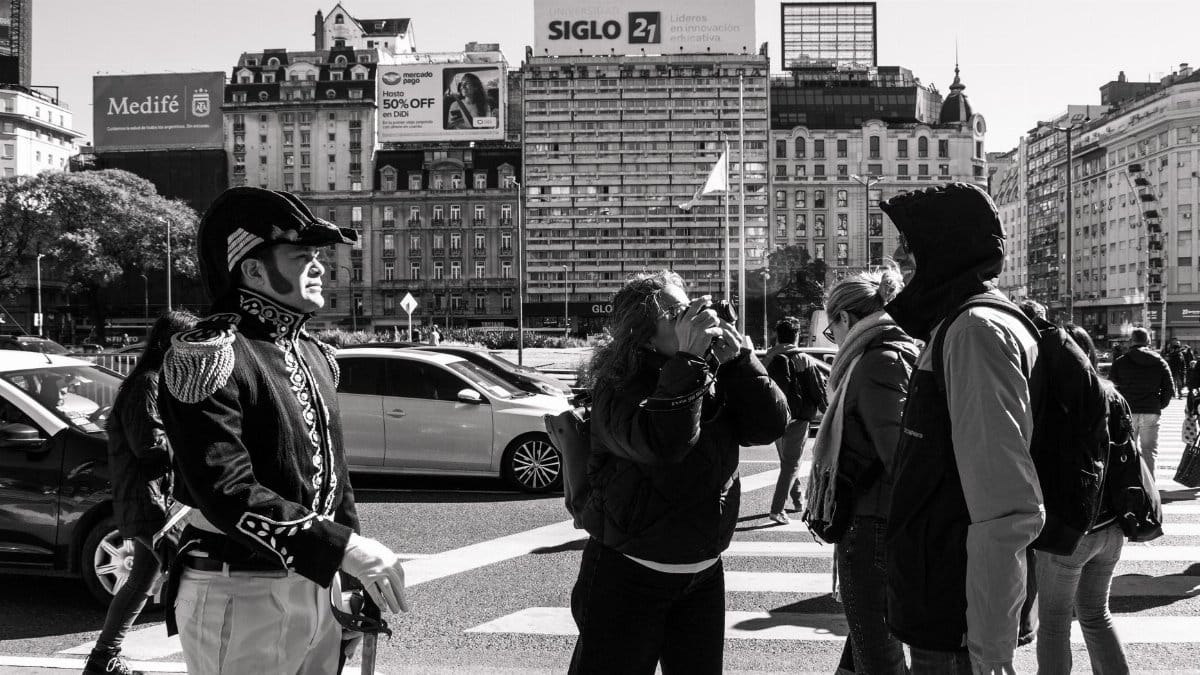 Black and white photo of a street performer in a historic costume amidst urban city life.