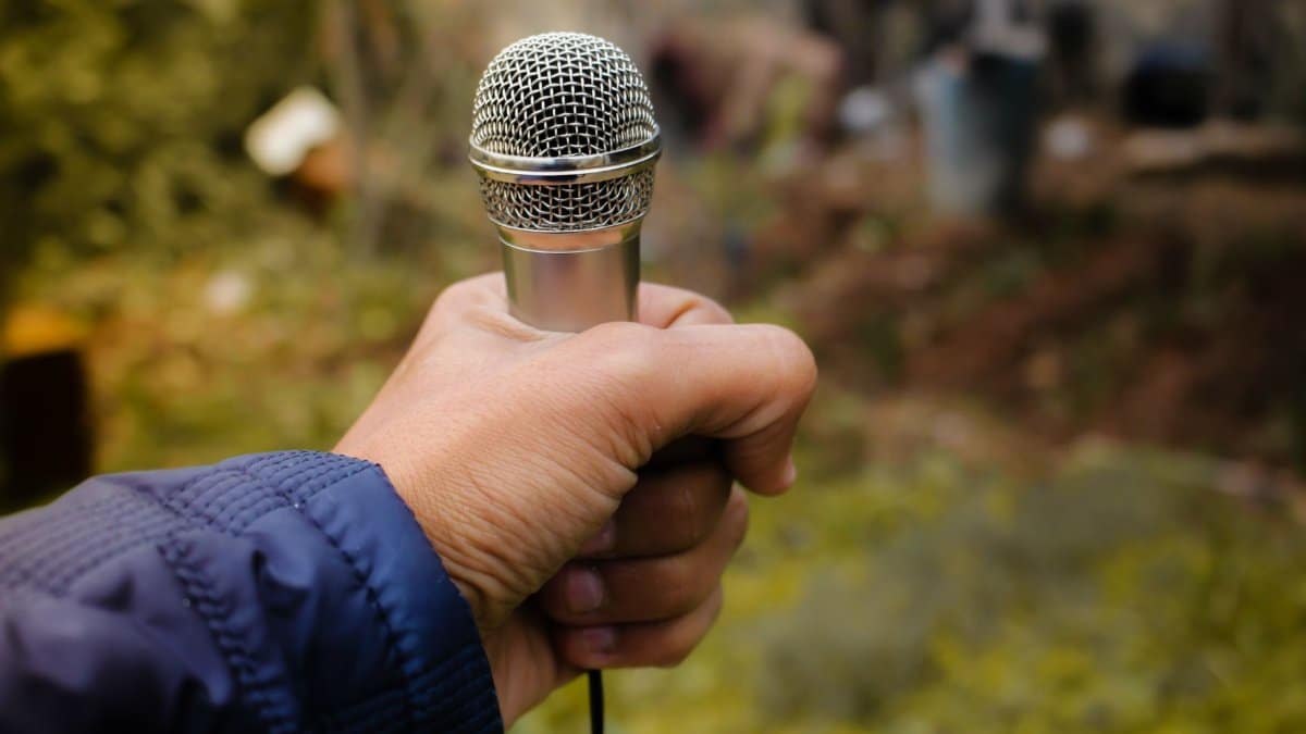A close-up of a hand holding a silver microphone in an outdoor environment, capturing focus and detail.
