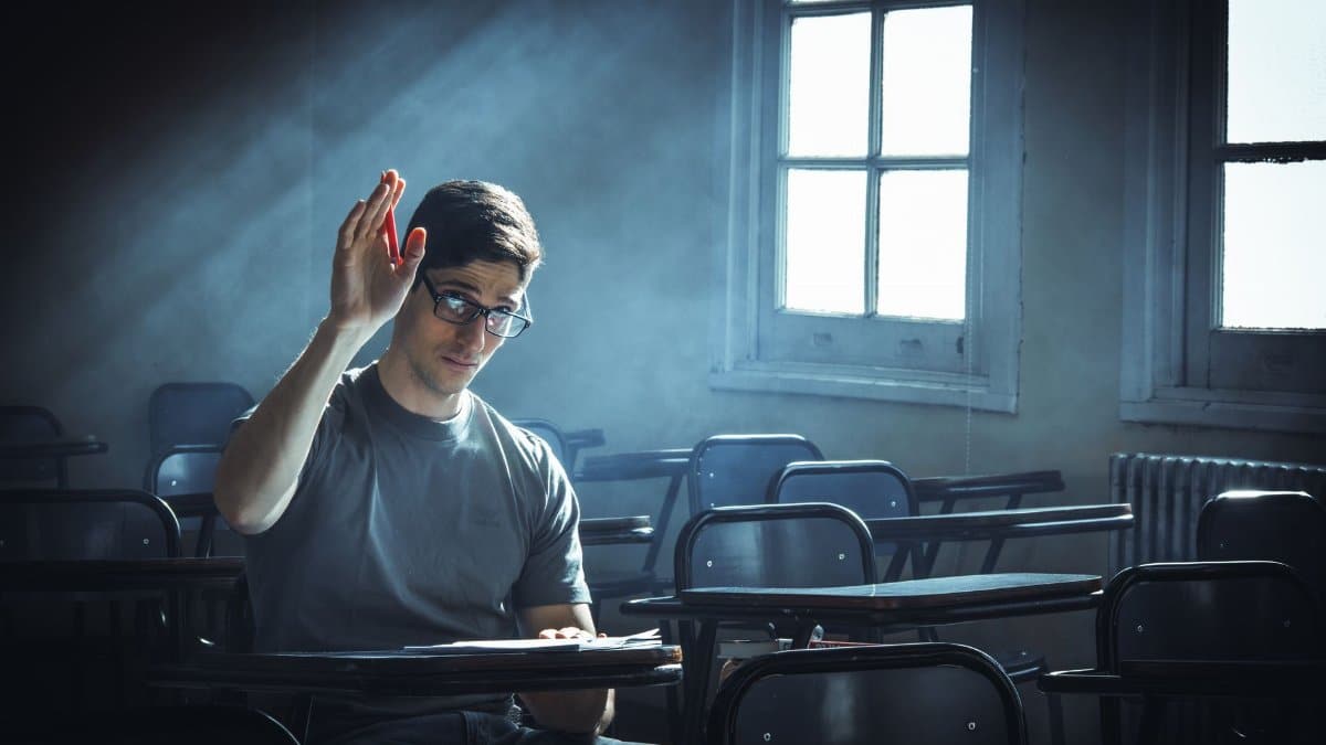 A student raises their hand in an empty classroom with dramatic lighting.