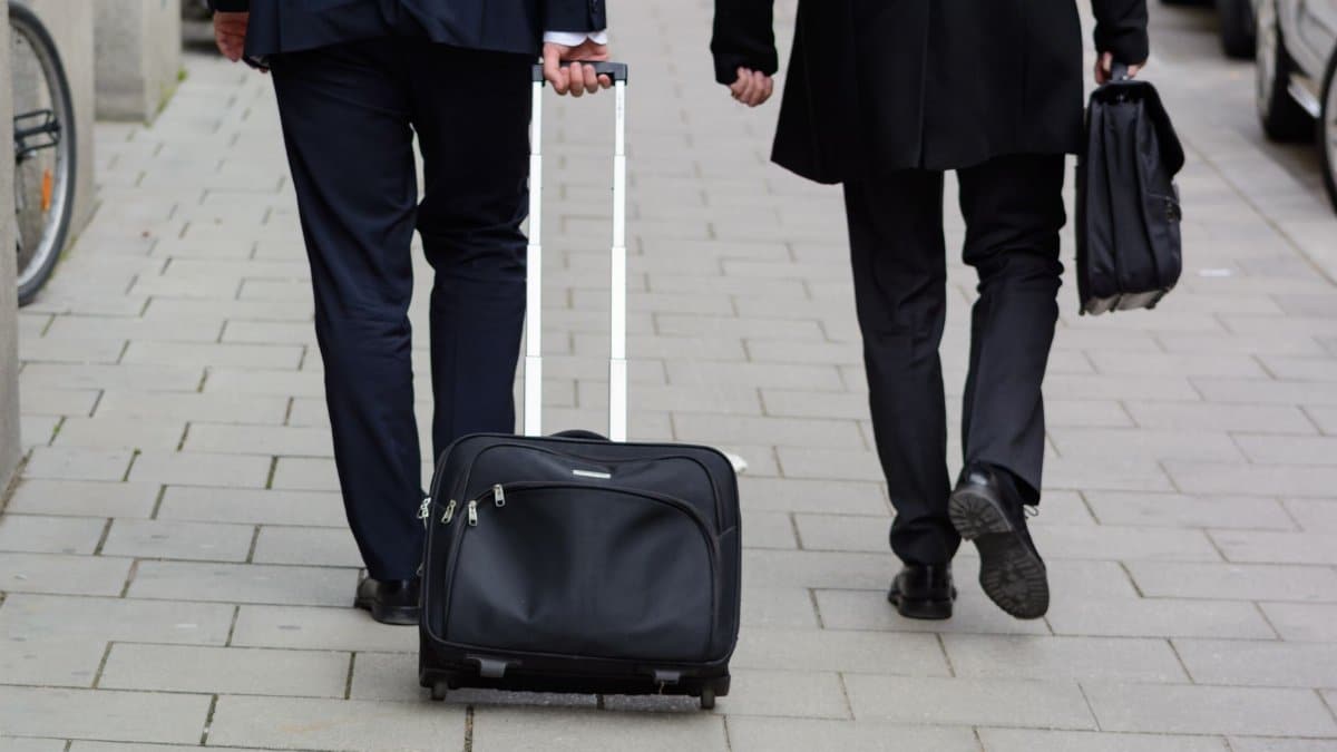 Two business professionals in suits walking on a Chicago street with luggage, showcasing urban lifestyle.