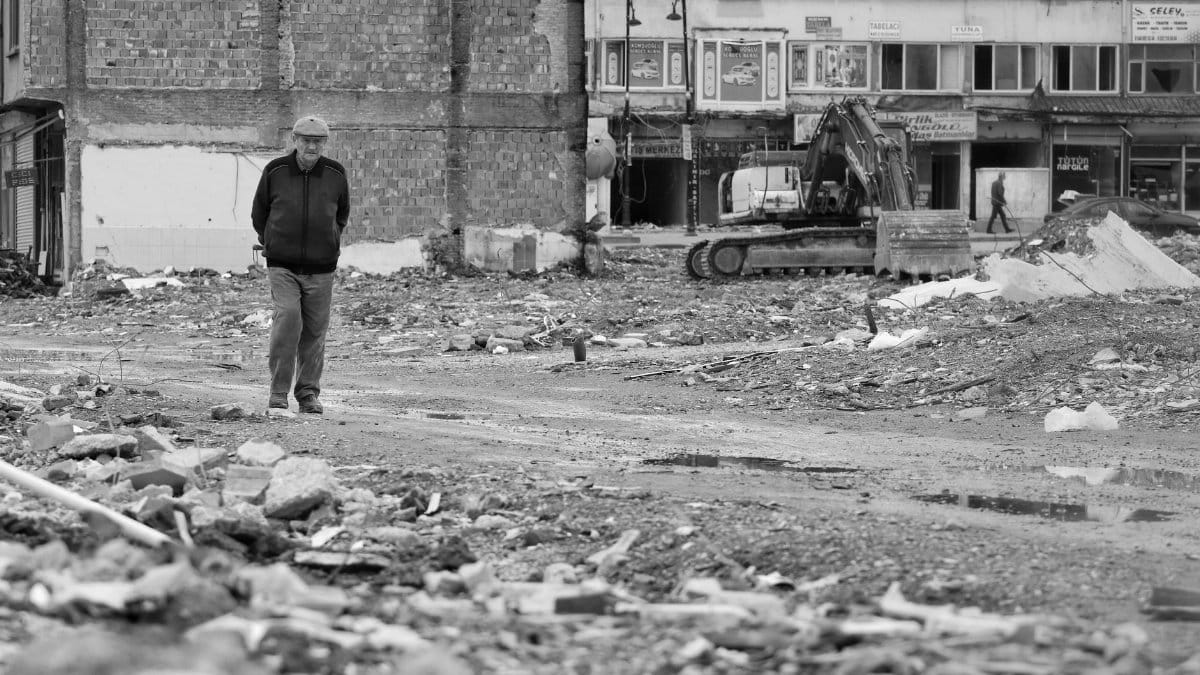 A man walks through ruins in a city, reflecting urban decay post-disaster.