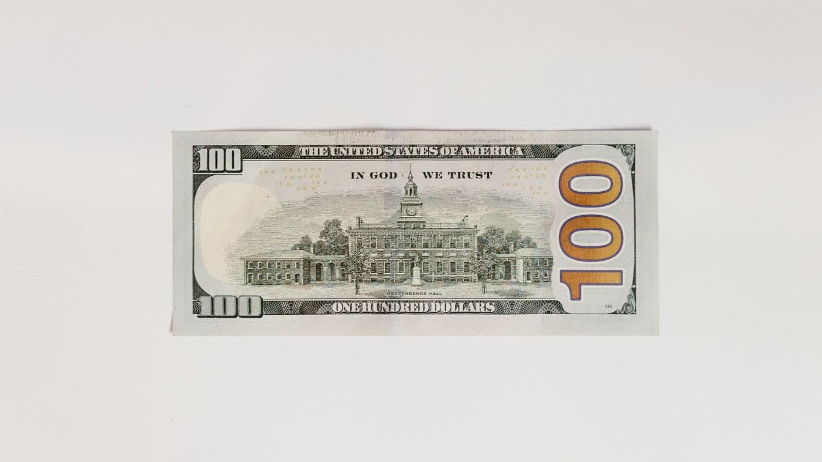 Close-up flatlay of a one hundred dollar bill against a plain white background.