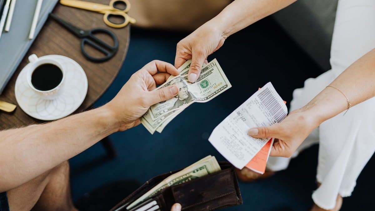 Close-up of a transaction with US dollar bills and receipts being exchanged over a table with coffee and scissors.