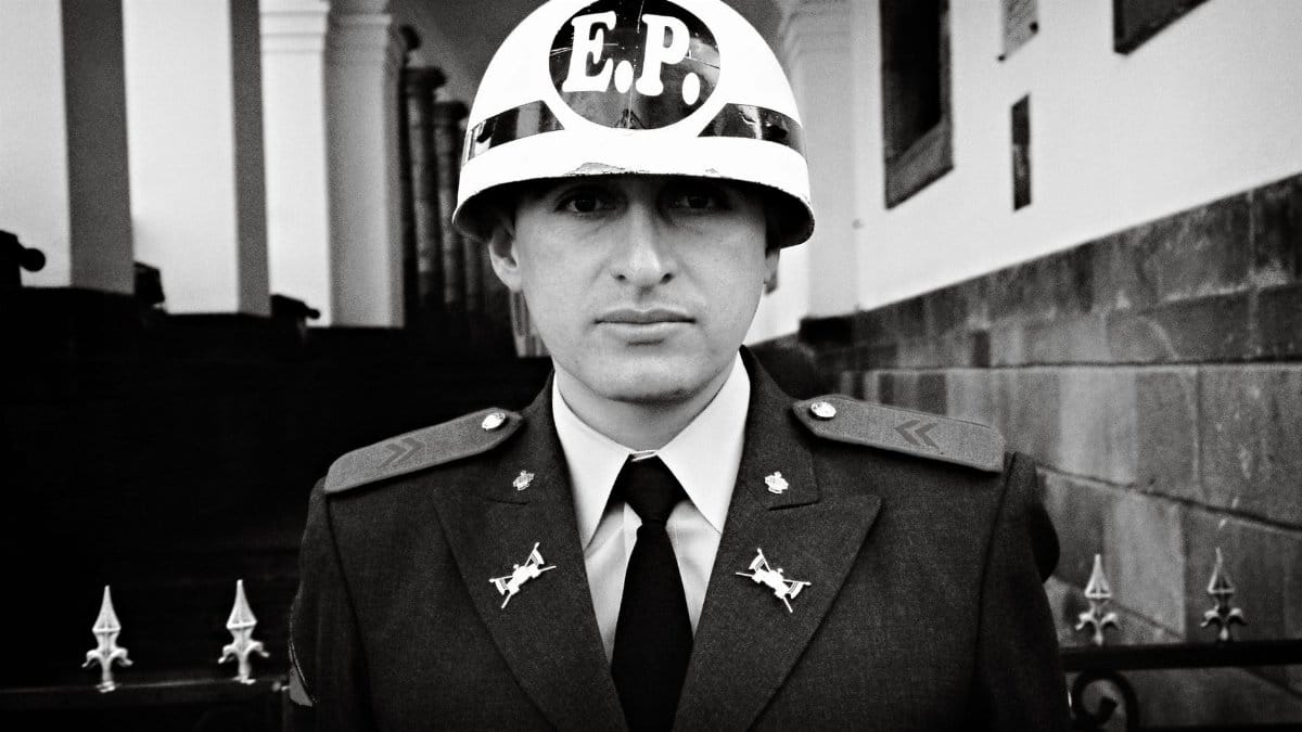 Black and white portrait of an Ecuadorian guard in uniform at a historical landmark in Quito.
