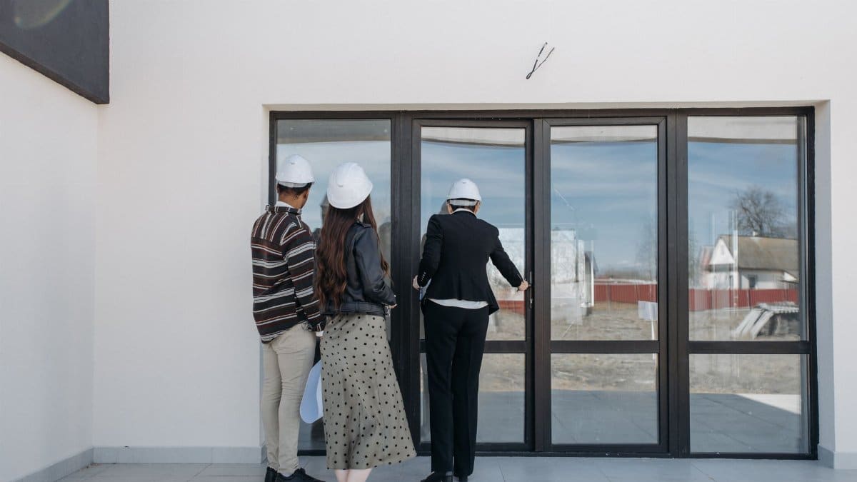 Real estate agents in helmets showing a new house to clients through glass doors.