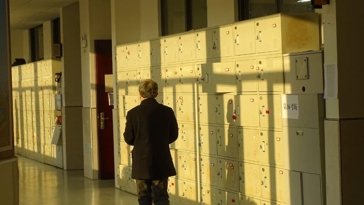 A person walks down a sunlit corridor filled with lockers, casting shadows on the wall.