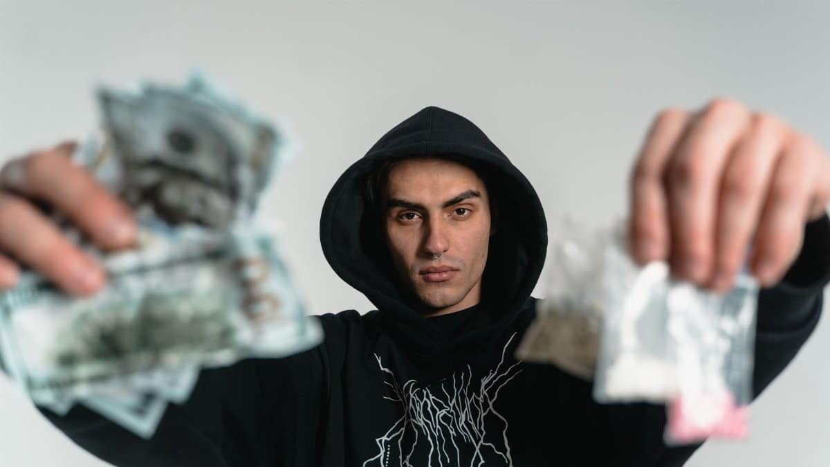 Close-up of a young man in a hoodie holding money and unidentified items, depicting urban life.