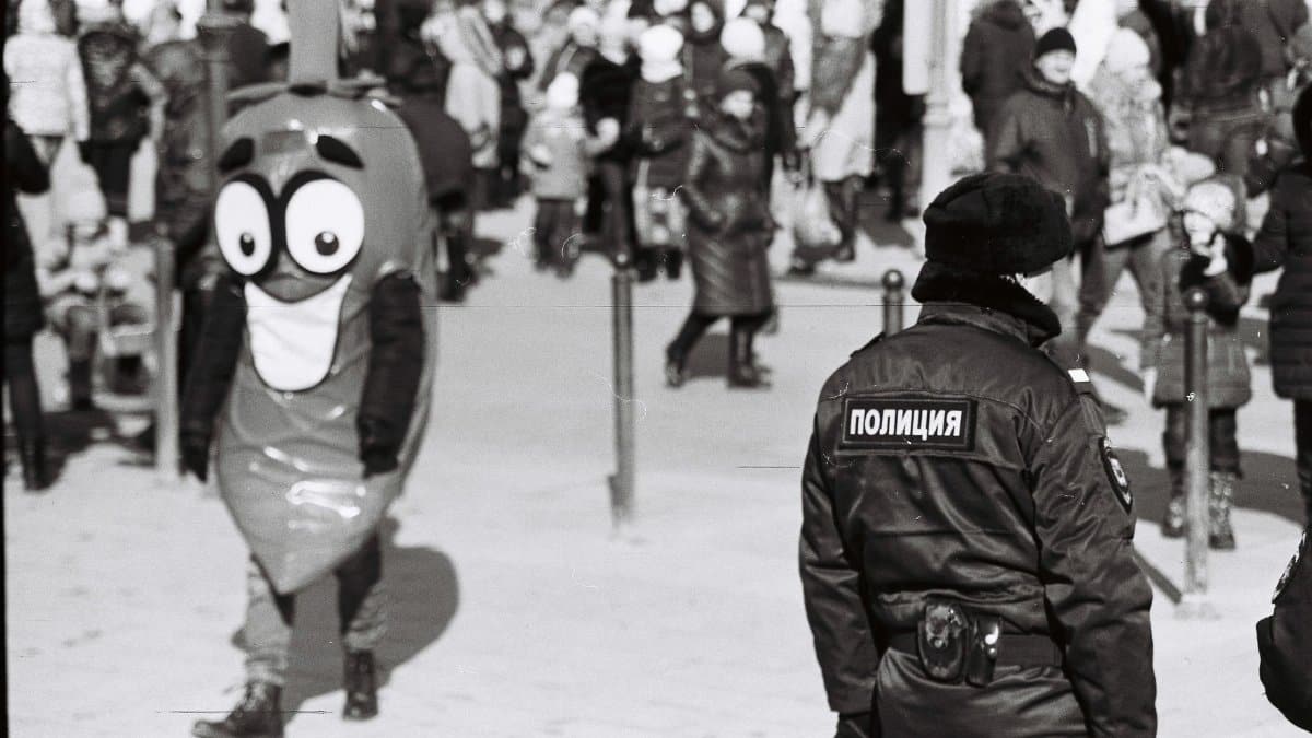 Grayscale street scene with a costumed character and a crowd in winter.