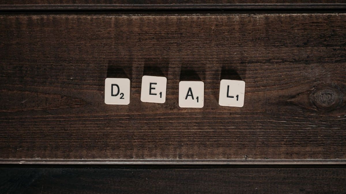 Scrabble tiles spelling 'DEAL' on a rustic wooden surface, viewed from above.