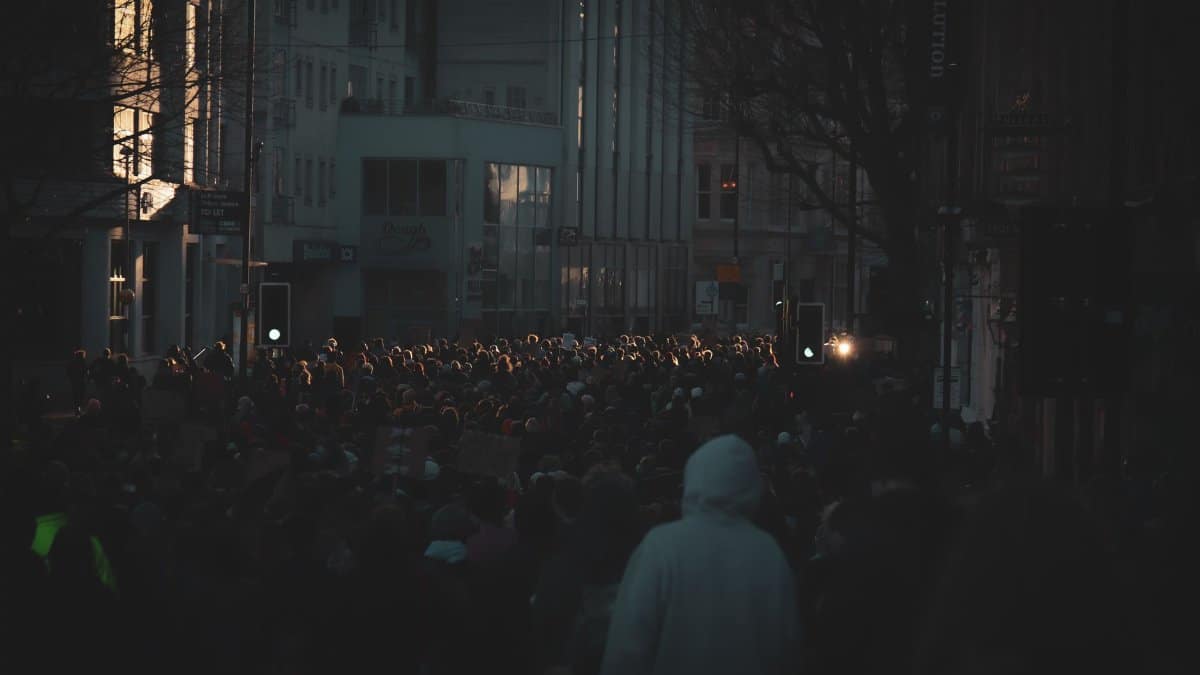A large crowd gathers for a protest rally on a dimly lit street in Bristol, England.