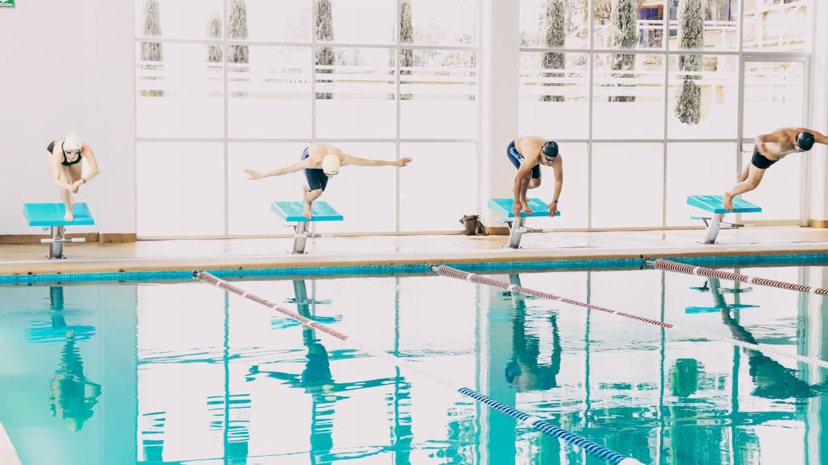 Swimmers poised on diving boards, ready to dive into an indoor pool during training.